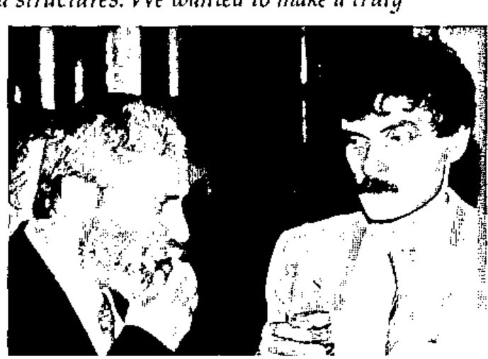 Two men in conversation, one bearded, one holding a glass