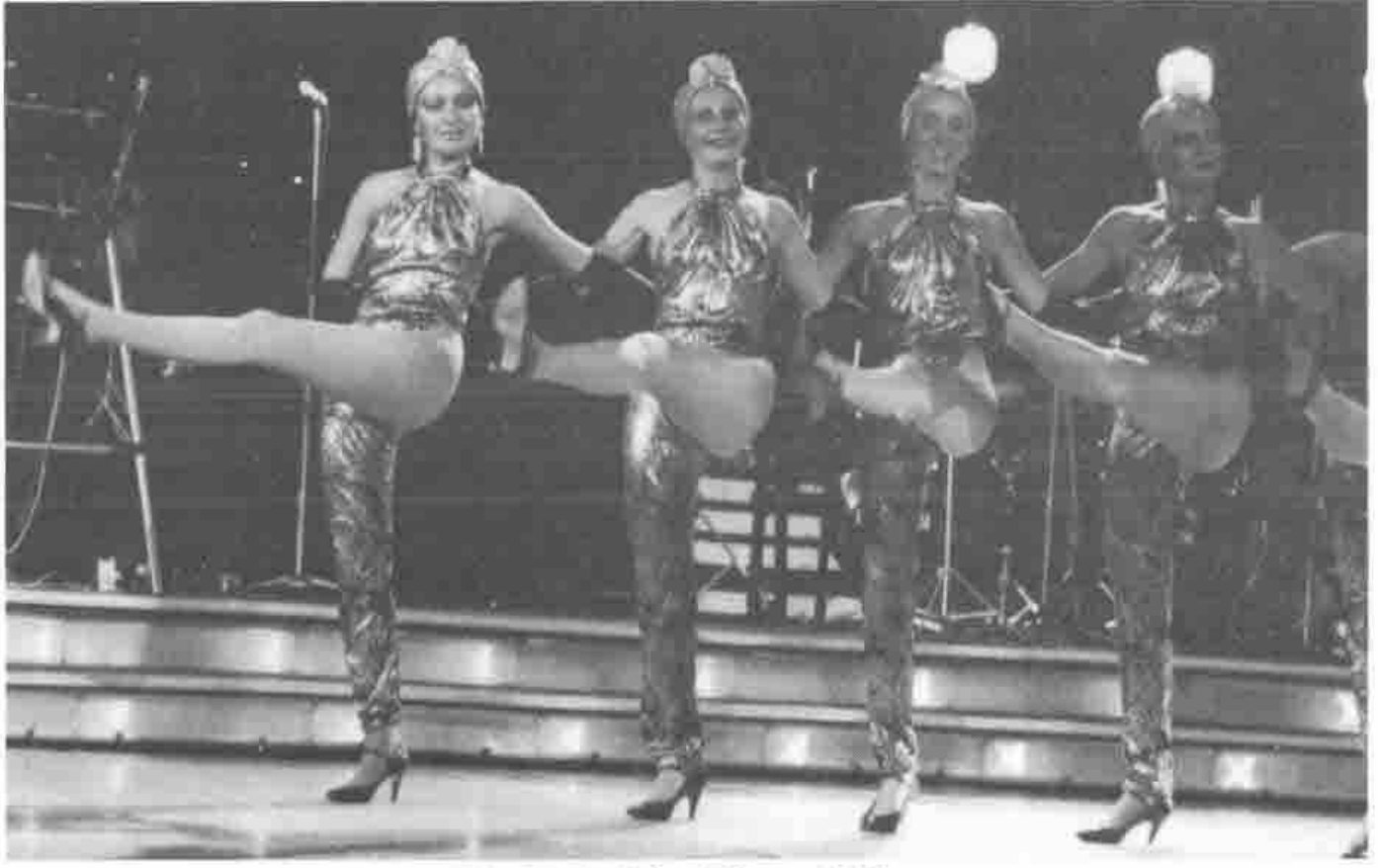 Four dancers in metallic costumes high-kicking in a line