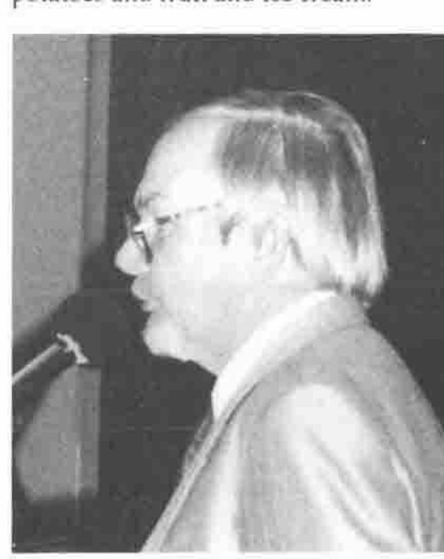 A white-haired man in glasses speaking at a microphone
