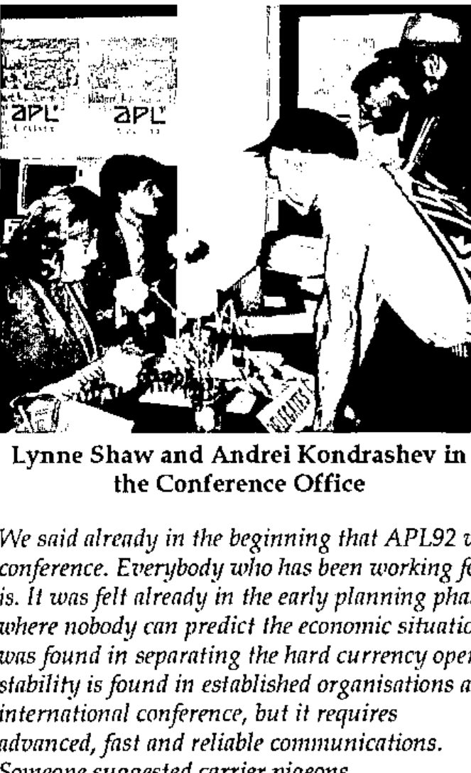 Two people at a table in an office, beneath APL posters