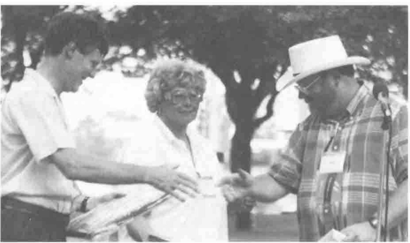 Peter Donnelly shakes hands with Mike Kent, who wears a cowboy hat; a woman stands between them