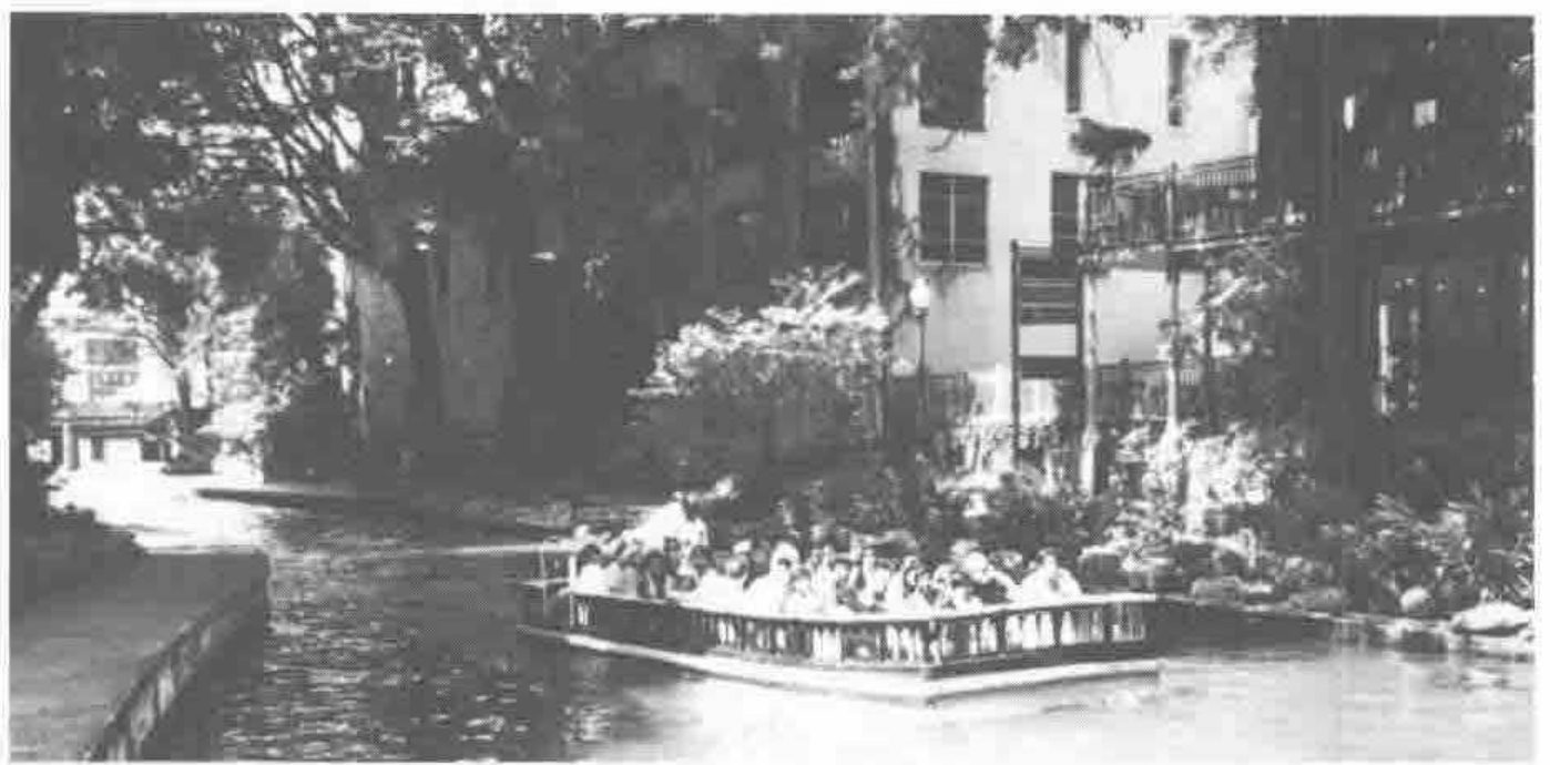 A tour boat full of passengers on the San Antonio river, under trees
