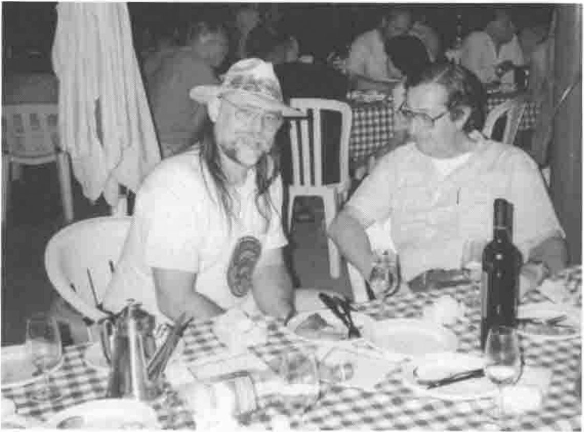 Bob Armstrong in a sun hat and Paolo Di Chio at a table with wine bottles and plates