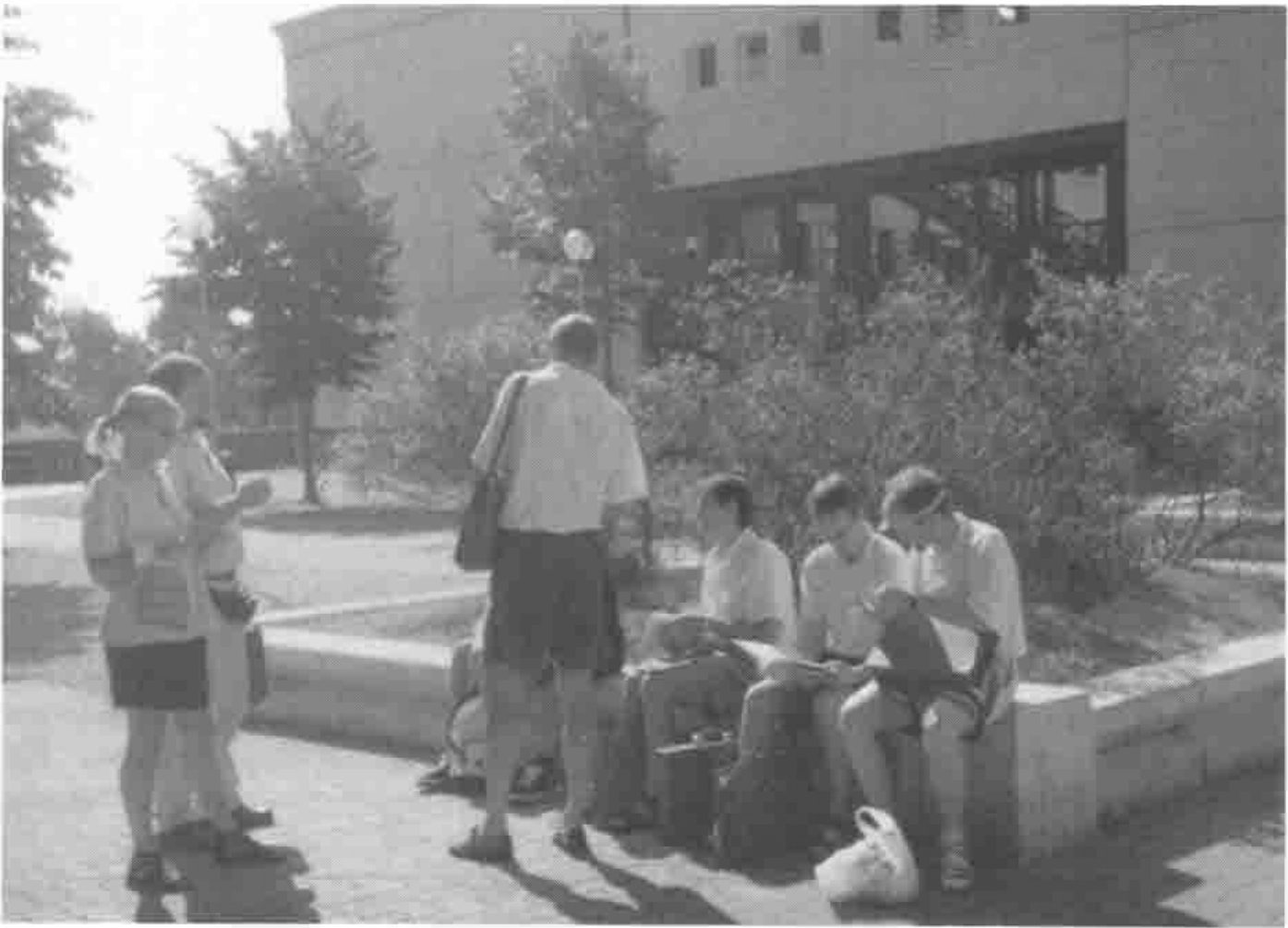 A group of delegates sitting and standing by a low wall in the sun outside a university building