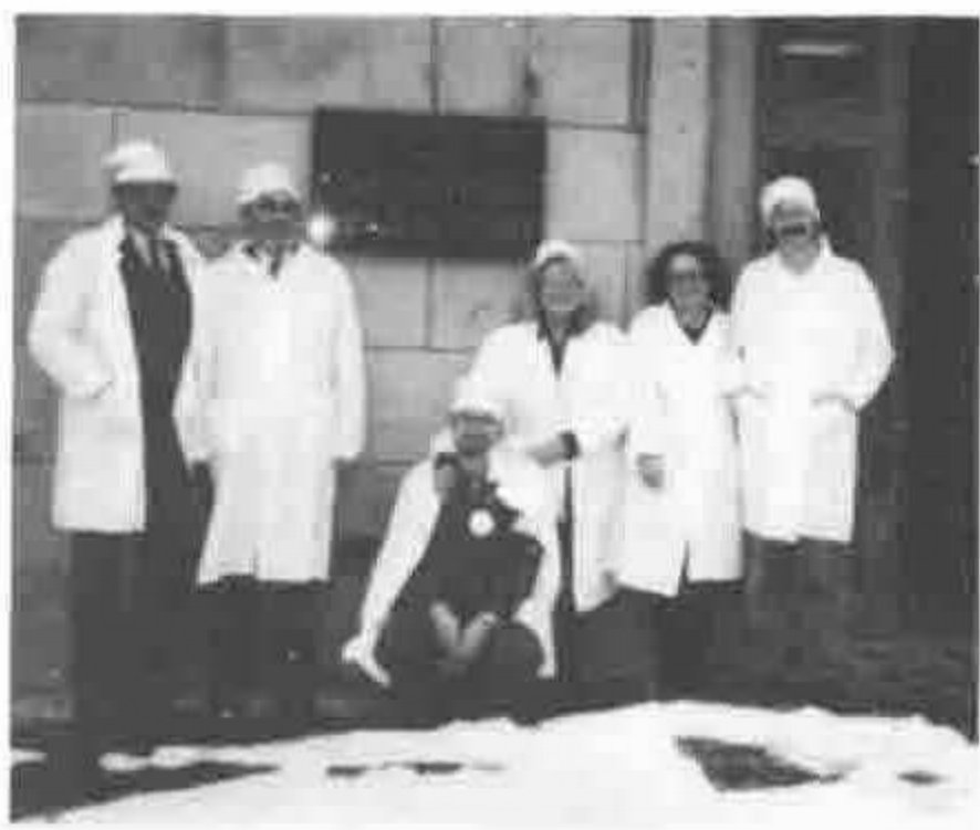 Six people in white coats and caps outside a stone building, in snow