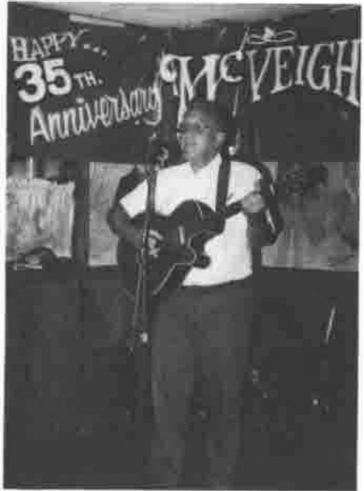 Jim Brown singing with a guitar under a banner reading Happy 35th Anniversary McVeigh’s