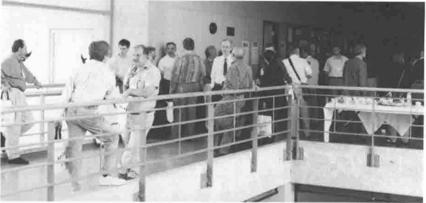 Delegates crowded on a first-floor landing with a rail, with coffee tables in the background