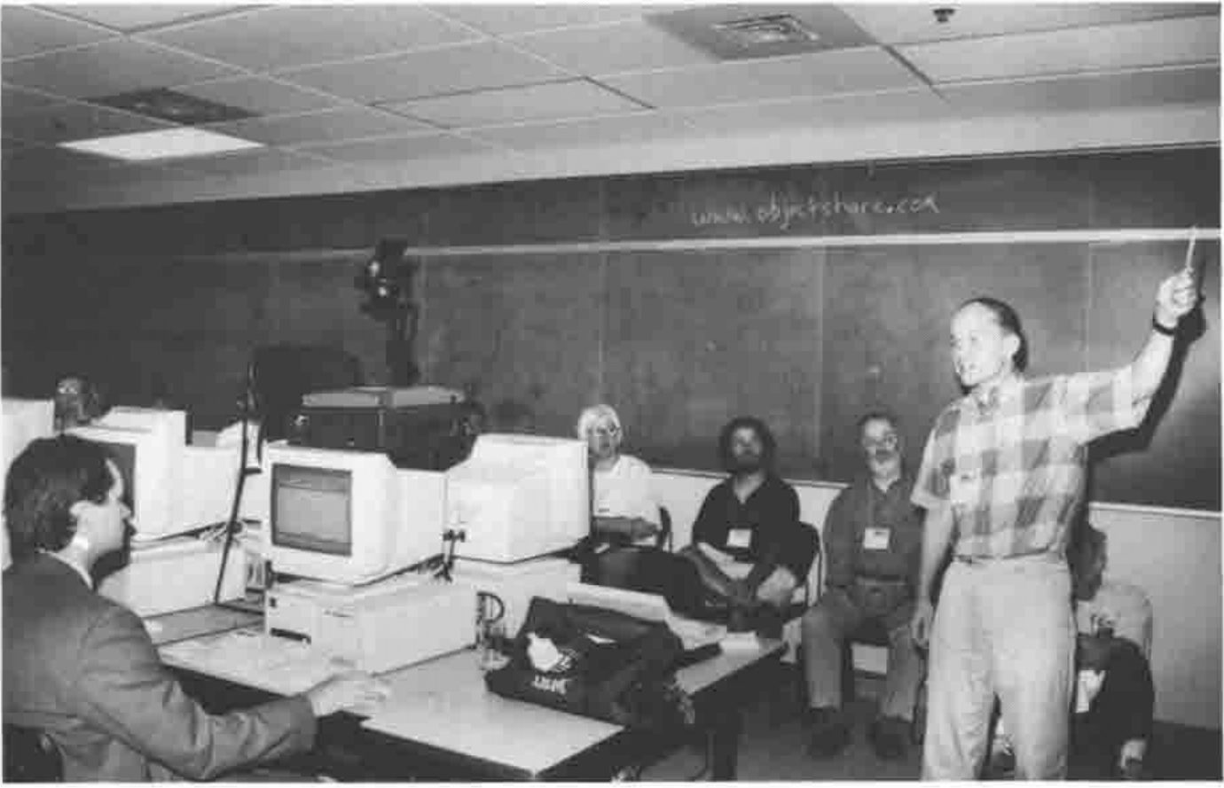 Timo Laurmaa pointing at a blackboard reading www.objectshare.com, with delegates at PCs