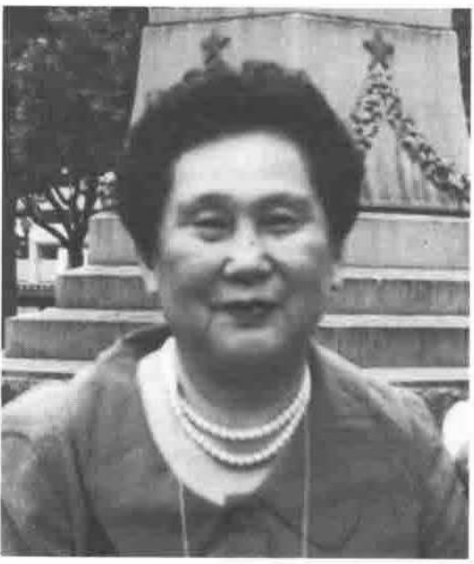 Photograph of Makoto Kikkawa, wearing a pearl necklace, in front of a stone monument