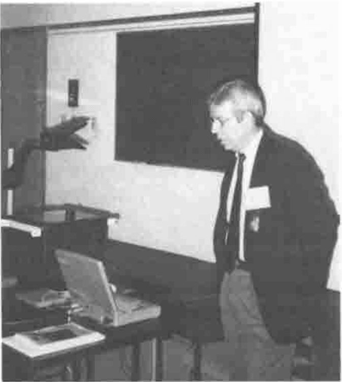 Photograph: Eric Lescasse gesturing towards a projection screen, beside a laptop