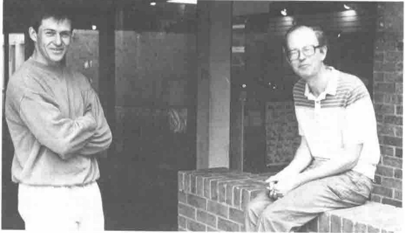 Photograph of Duncan Pearson, standing with arms folded, and Adrian Smith, seated on a low brick wall