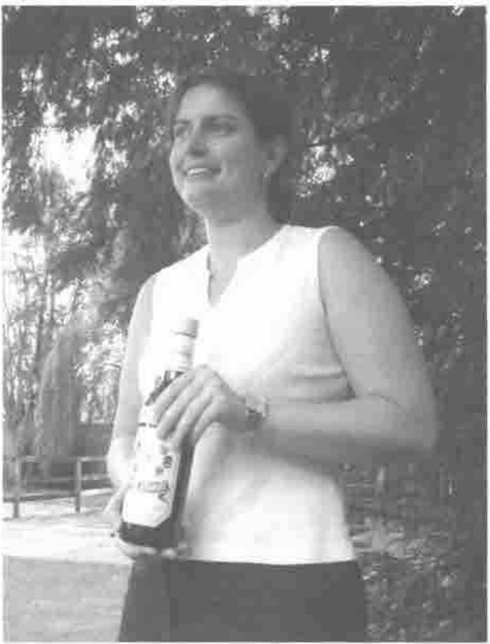 A smiling woman holding a bottle of Aalborg Akvavit, under a tree