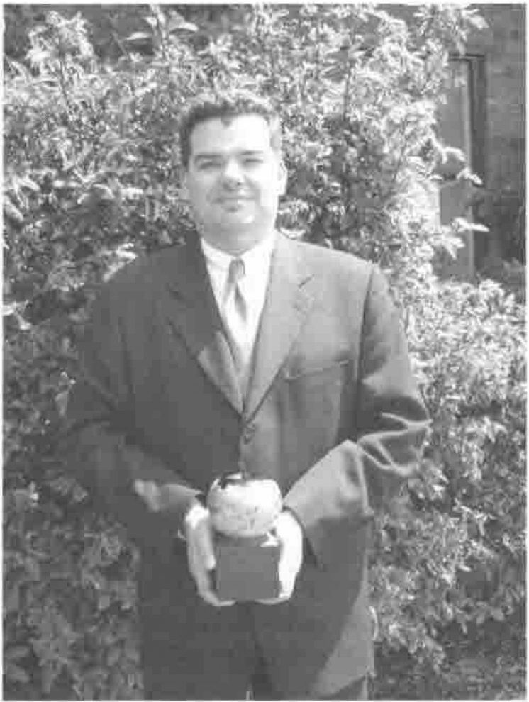 John Daintree, in a suit, holding the award in front of a hedge