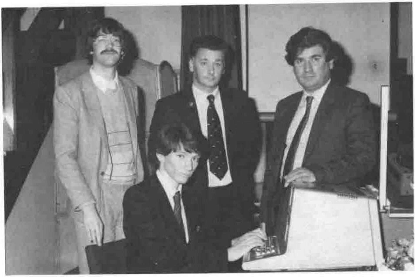 Photograph: four men, one seated at the TRS 80 computer