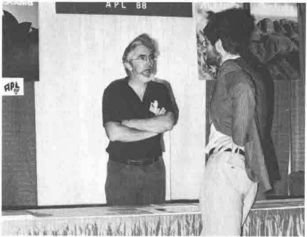A man with folded arms talking to another man in front of an APL 88 stand