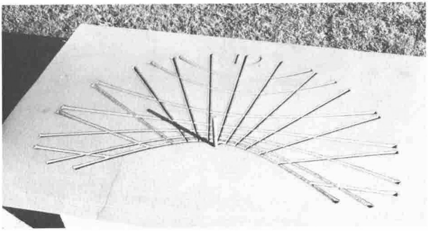 A pale slab on grass with a fan of rods radiating from one point, like the hour lines of a sundial; one rod is darker than the rest