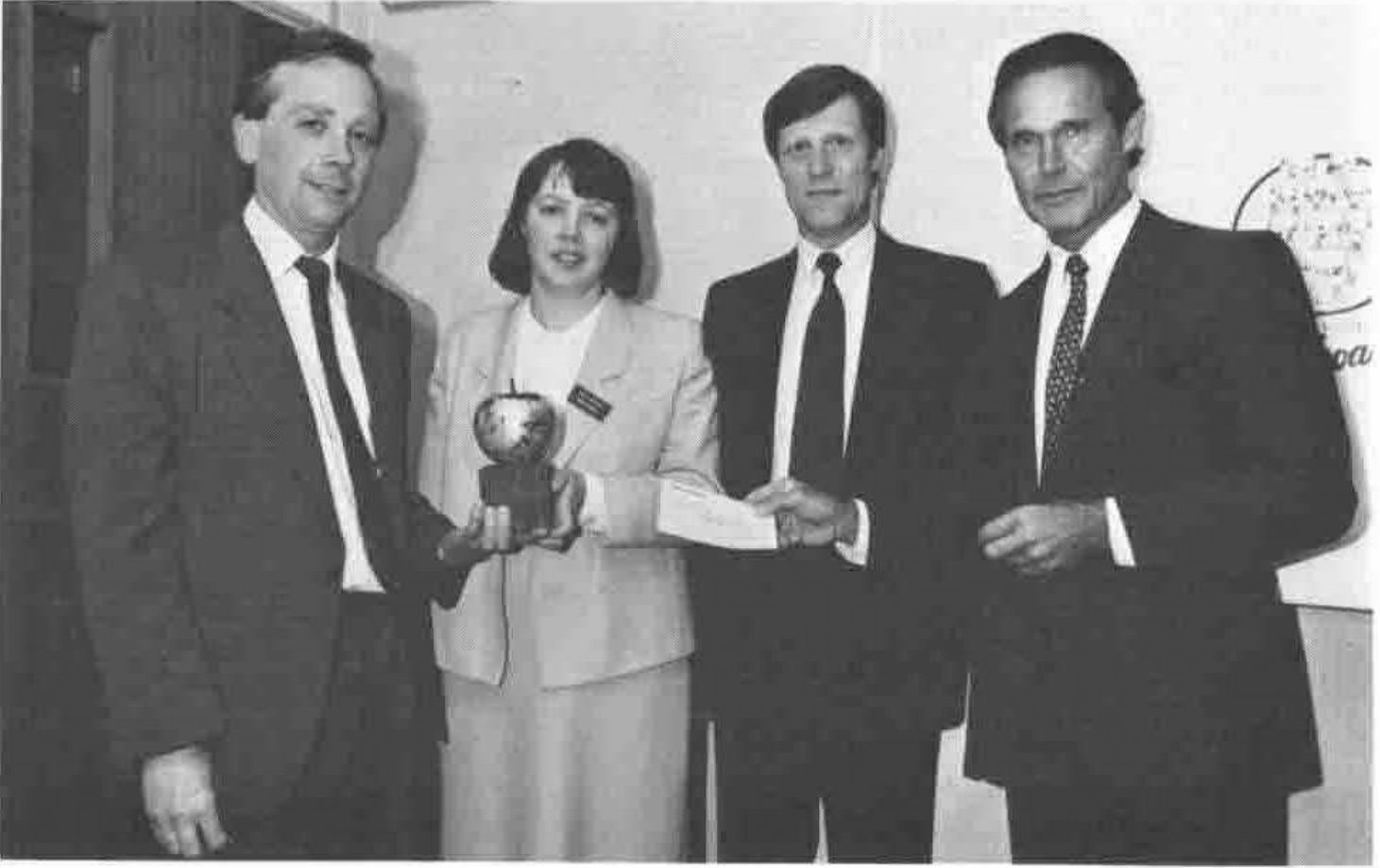 Four people at the award presentation; one holds the apple-shaped trophy, another hands over an envelope