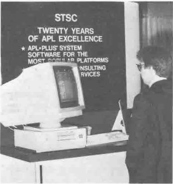 Photograph of the STSC stand: a PC in front of a banner reading “STSC — Twenty years of APL excellence — APL*PLUS System software for the most popular platforms … consulting services”, with a visitor