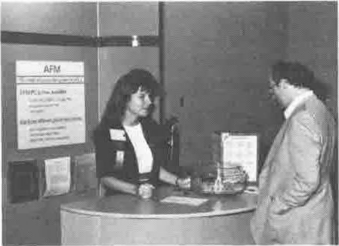 Photograph of the AFM exhibition stand: a woman behind the counter talks to a visitor, with AFM posters on the wall behind