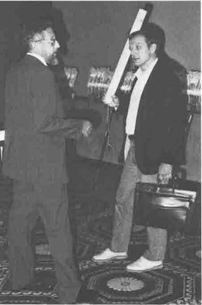 Photograph of Lee Dickey, holding a long cardboard tube, talking with A.K. Dewdney