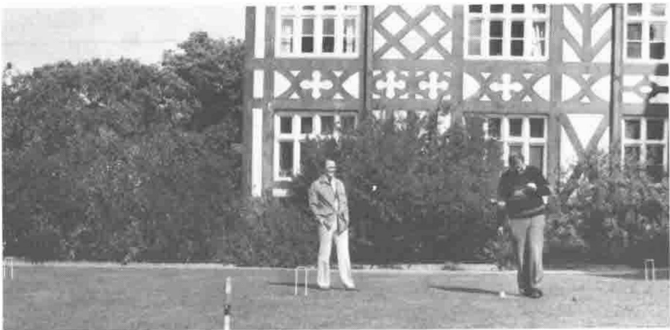 Photograph of two men playing croquet on a lawn in front of the hall