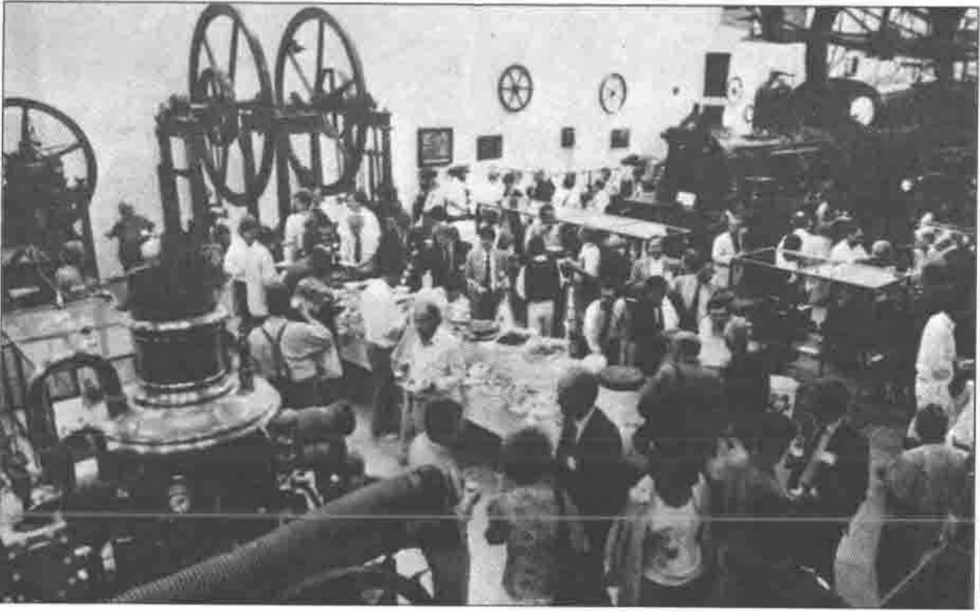 A crowded reception among large machines and flywheels in a museum hall
