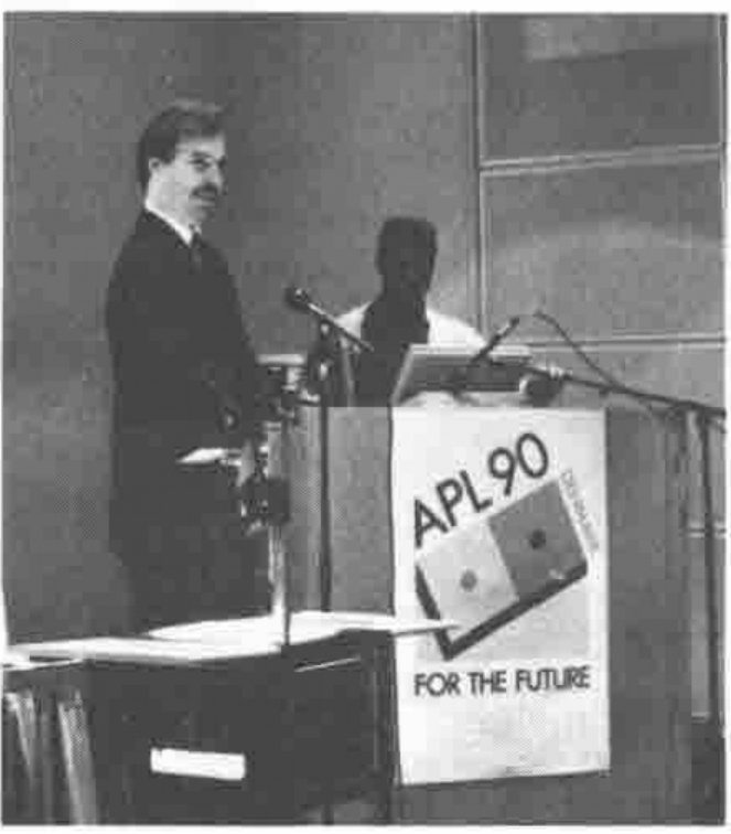 Two men, one standing beside a lectern bearing an “APL 90 For the Future” poster