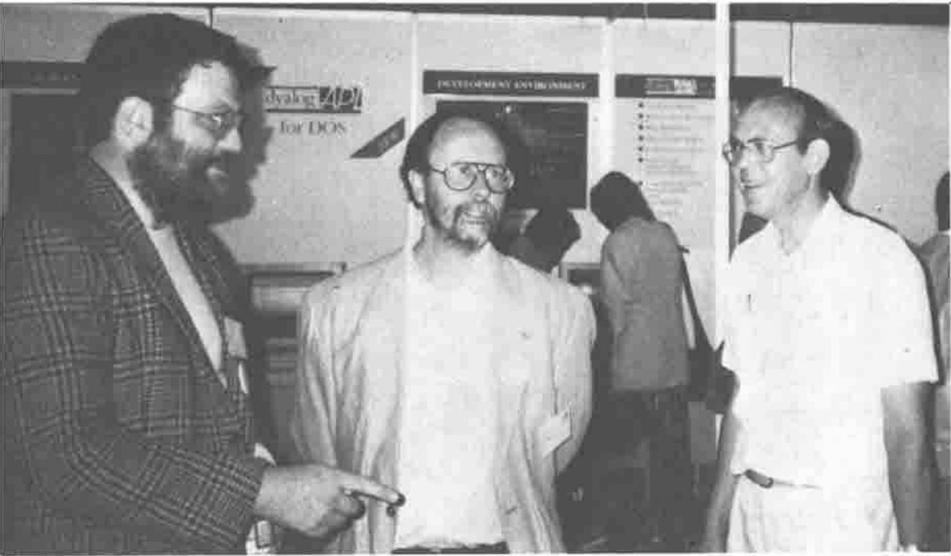 Three men talking in front of a Dyalog APL for DOS display