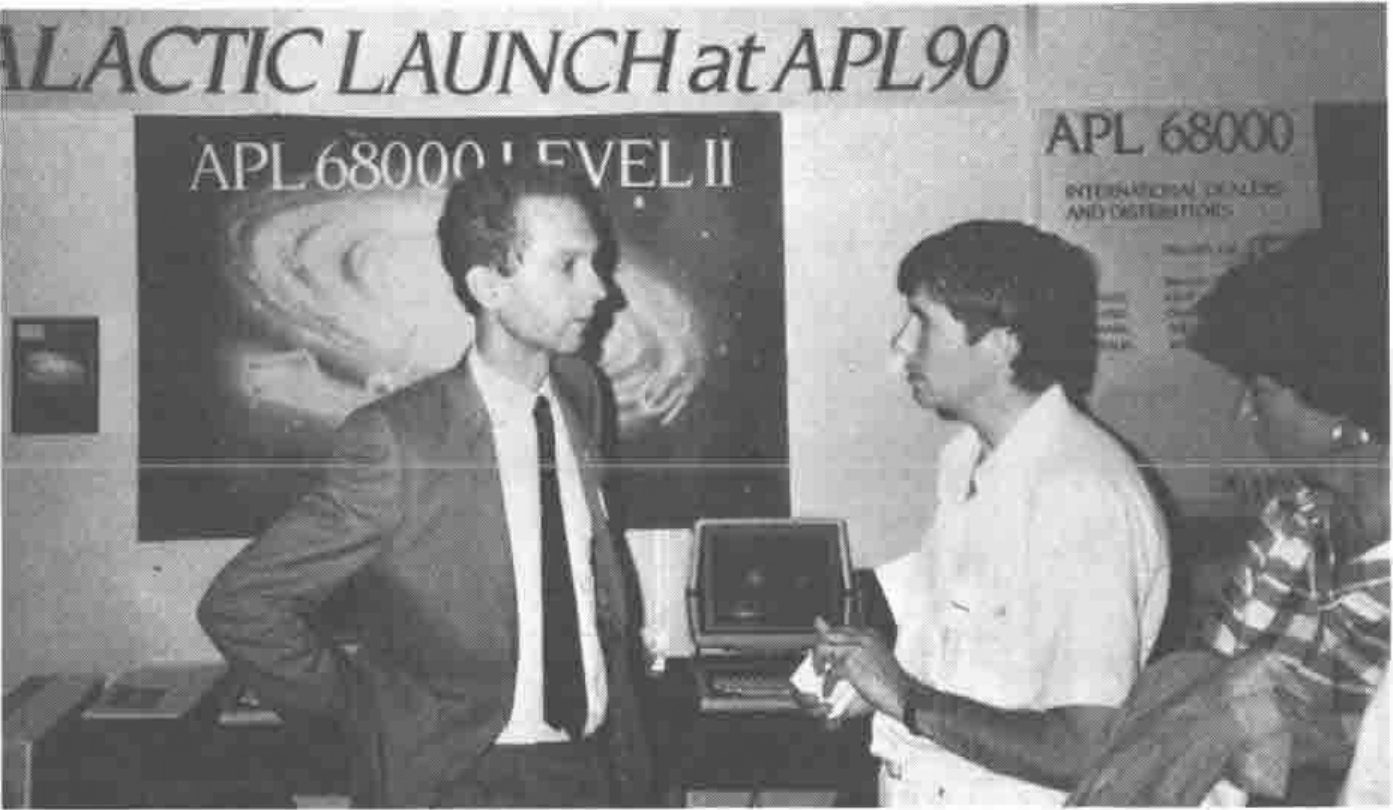 Two men talking beneath a banner reading “…LACTIC LAUNCH at APL90” and a poster for APL.68000 Level II