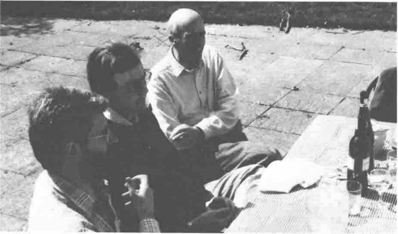 Three men talking at an outdoor table with a wine bottle