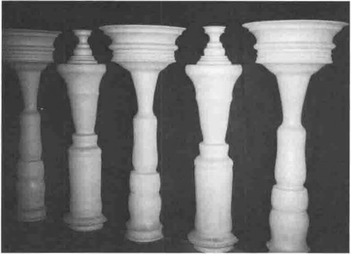 A row of white turned vases against a dark background; the gaps between them form the profiles of faces