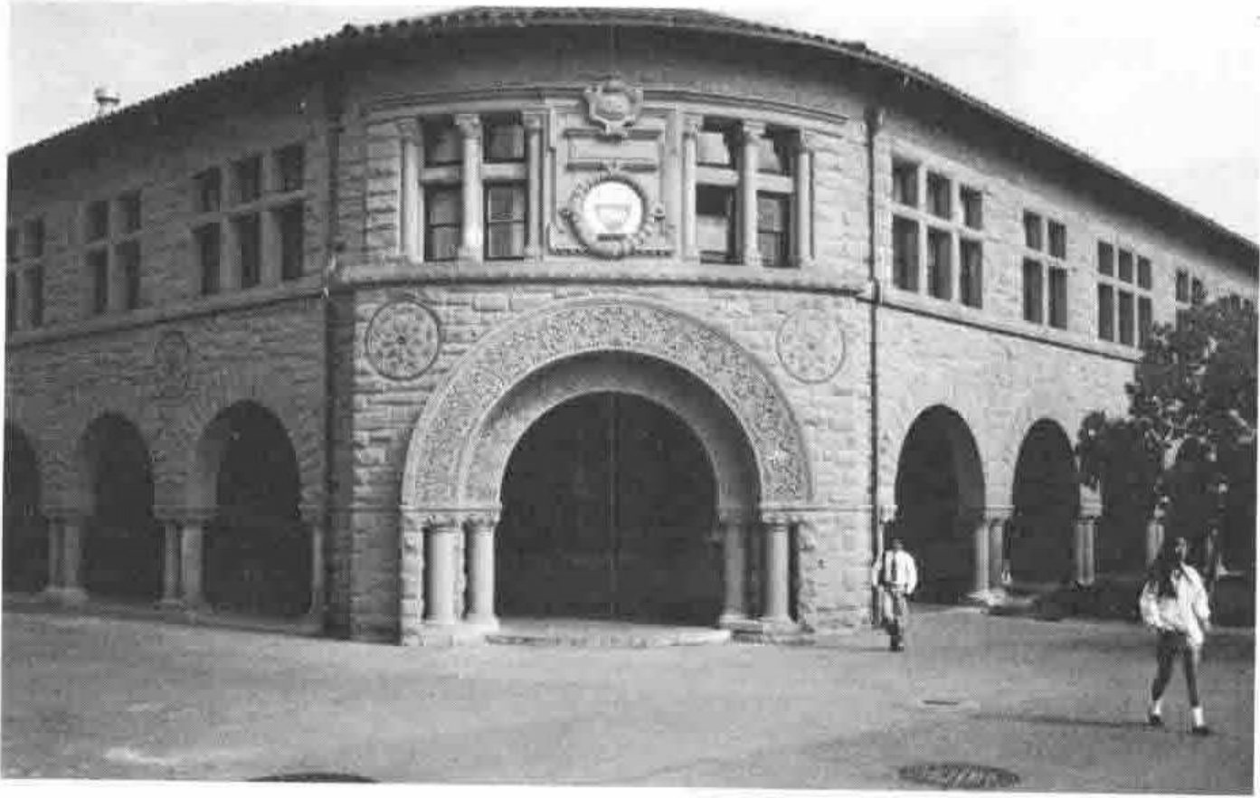 A corner of a sandstone building at Stanford, with a carved archway and an arcade of round arches