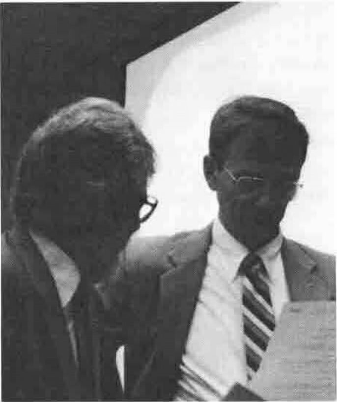 Two men in jackets and ties, one in glasses looking at papers