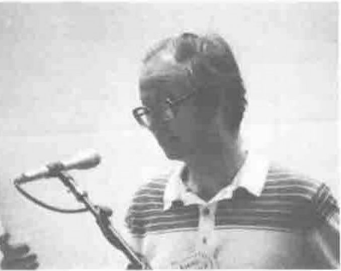 A man in glasses and a striped shirt speaking into a microphone