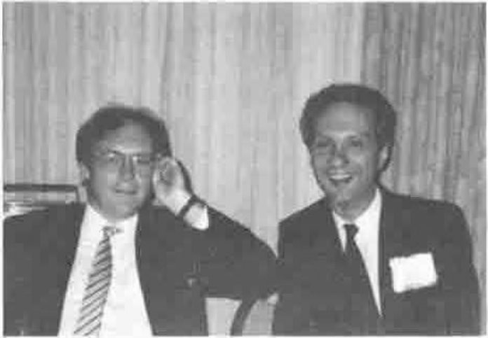 Two men in suits, smiling, one with his hand to his ear