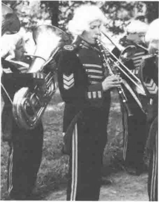 Bandsmen in braided uniforms and white powdered wigs playing brass instruments and a clarinet
