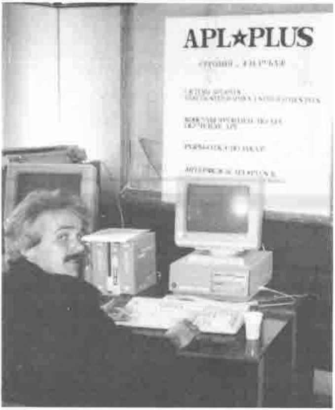 A man seated at a PC, looking over his shoulder, beneath a poster headed “APL★PLUS” with text in Russian